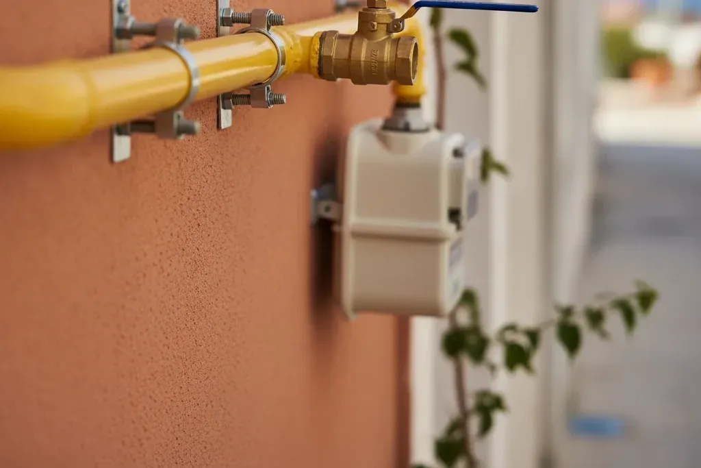 Duvara sabitlenmiş sarı doğalgaz borusu, küresel vana ve sayaç bağlantısı